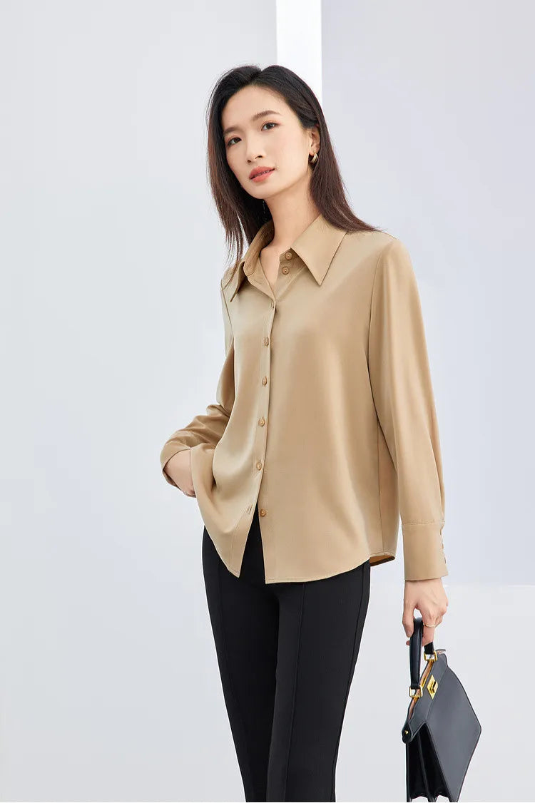 Woman wearing a beige blouse and black pants holding a black handbag against a white background
