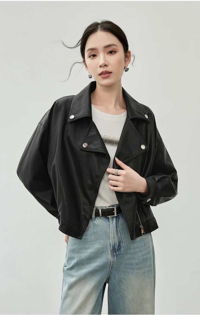 Person wearing a black leather jacket and light blue jeans on a plain background