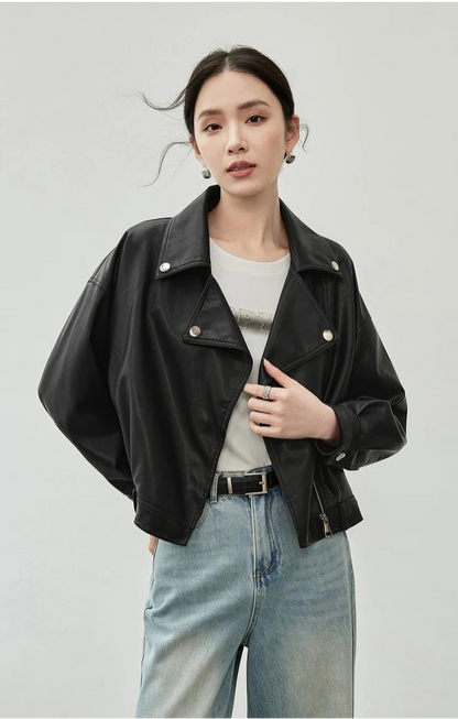 Person wearing a black leather jacket and light blue jeans on a plain background