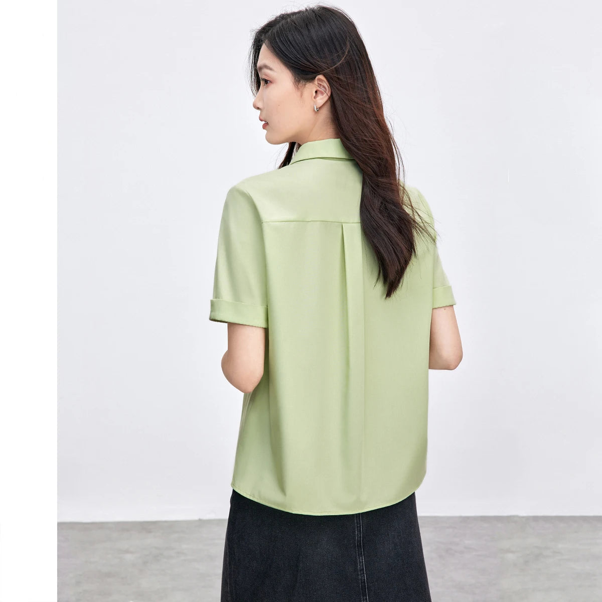 Woman wearing a light green shirt with a plain background.