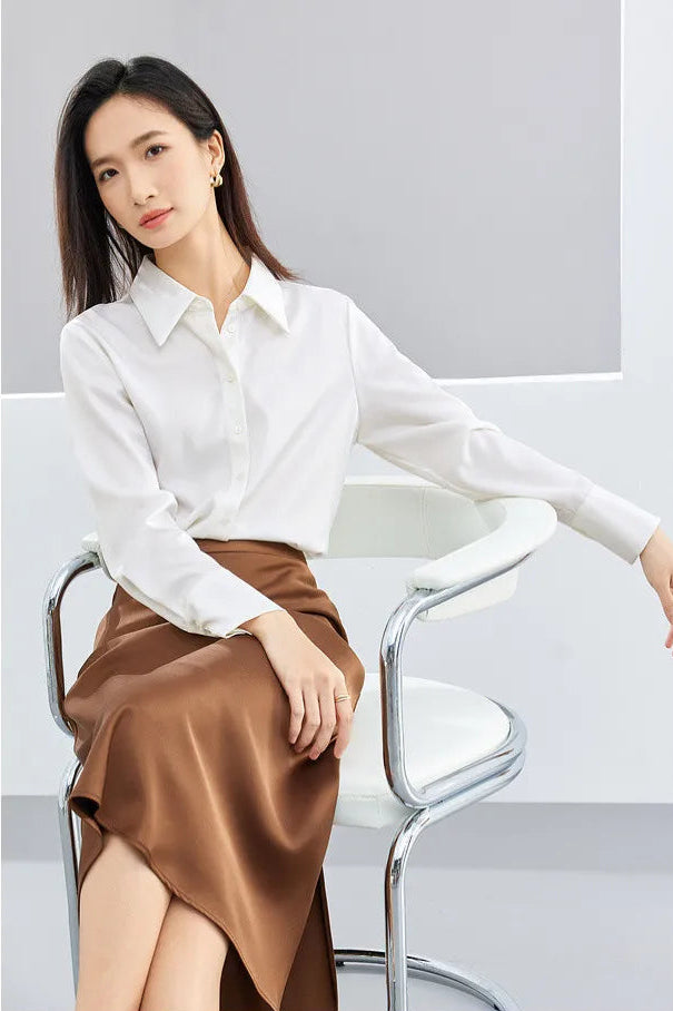 Woman wearing a white blouse and brown skirt sitting on a chair against a gray background